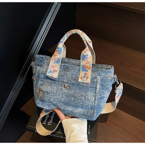 Detail of blue denim tote bag with floral pattern straps and silver metal snap closure