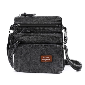 Close-up of black denim crossbody bag with multi-layer zippers and leather logo detail