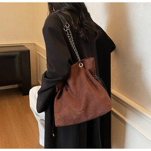 Détail du sac seau en daim marron foncé avec bandoulière chaîne et fermeture cordon
