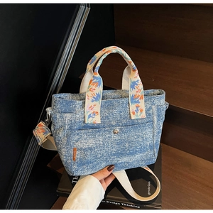 Detail of blue denim tote bag with colorful floral embroidery on the carry handle