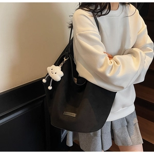 Detail of black suede hobo tote bag featuring fashion metal label and cloud plush charm