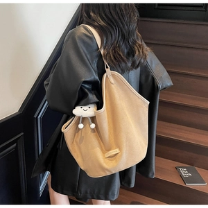 Khaki suede tote bag with plush charm shown from the back on a model in black leather jacket