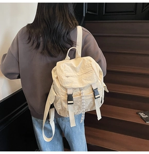 Creamy nylon backpack with flap closure and black buckles on model's back outdoors