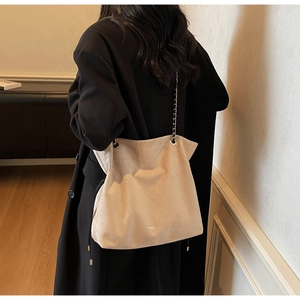 Détail du sac cabas beige en daim avec chaîne argentée porté sur un manteau noir