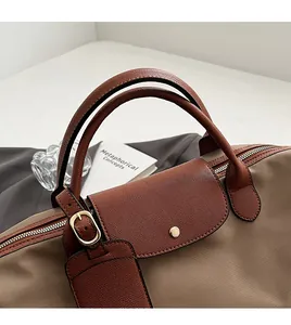 Close-up of beige nylon tote bag featuring brown leather flap and golden metal buckles