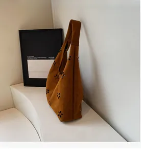 Detail of brown suede tote bag featuring intricate laser-cut floral patterns and texture