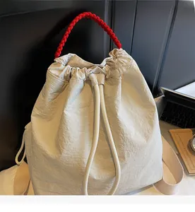 Dettaglio della borsa a secchiello crema con manico intrecciato rosso e coulisse