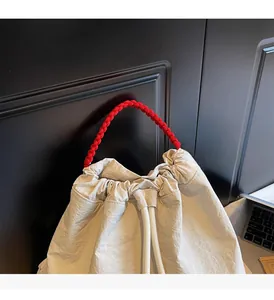 Dettaglio borsa a secchiello beige con coulisse, manico intrecciato rosso e tessuto