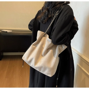 Détail d'un sac fourre-tout en daim beige doux avec bandoulière chaîne porté par un mannequin