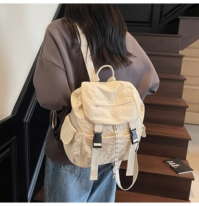 Detail view of cream nylon backpack with buckle closure on dark wooden stairs background