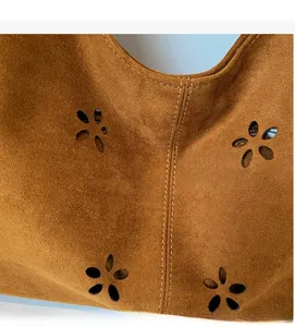 Close-up detail of brown suede fabric with hollowed flower pattern and fine stitching on bag