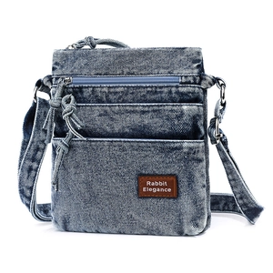 Close-up of washed denim crossbody bag showing multi-layered zipper pockets and fabric texture