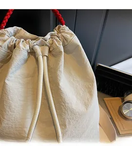 Dettaglio dello zaino beige con coulisse e manico rosso su una scrivania con un laptop