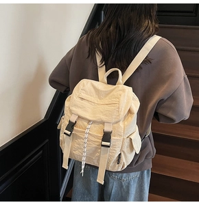 Close-up of cream nylon backpack with black buckle closure and side pocket detail