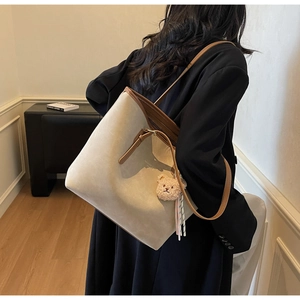 Side view of cream tote bag with brown leather trim and cute bear charm on model