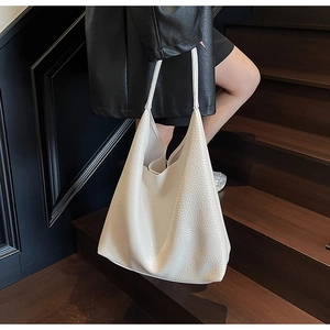 Detailed texture of off-white leather tote bag shown on a model on wooden stairs
