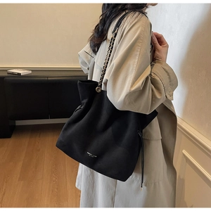 Détail du sac seau noir en daim avec bandoulière chaîne métallique et cordon serrage