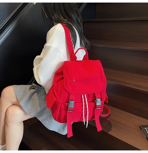 Red nylon backpack with dual buckle flap and drawstring detail on wooden stairs