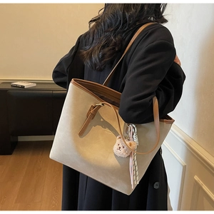 Rear view of a large beige tote bag with brown leather trim and a cute teddy bear charm