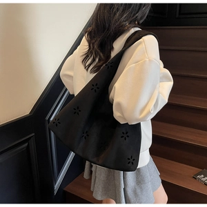 Detail view of large black laser-cut floral tote bag shown on a shoulder in a casual setting