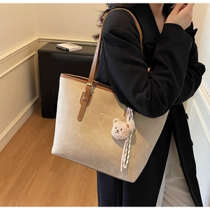 Detail of a beige tote bag with brown leather trim and a cute plush bear charm accessory