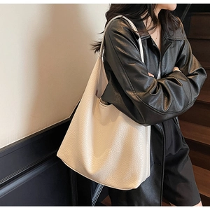 Close-up of cream white lychee texture leather tote bag worn by a model in black leather jacket