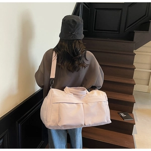 Model showing a large pale pink travel bag with shoulder strap in a minimalist setting