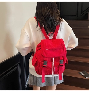 Detalle de mochila de nailon roja con hebilla negra y cordón en la espalda del modelo