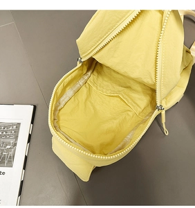 Interior detail of yellow nylon chest bag showing white zipper and internal pocket