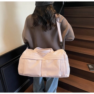 Detail of pink travel duffel bag with front pockets on model by wooden stairs