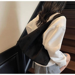 Detail of black tote bag with laser-cut flower patterns worn by a model on a shoulder