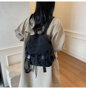 Detail of black nylon backpack featuring flap closure, dual buckles, and drawstring design