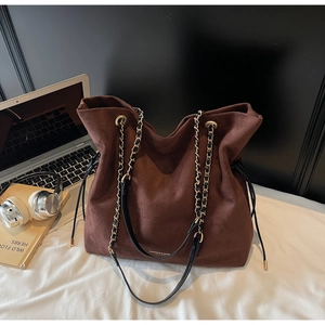Détail du sac seau en daim marron foncé avec chaîne dorée et cordon latéral