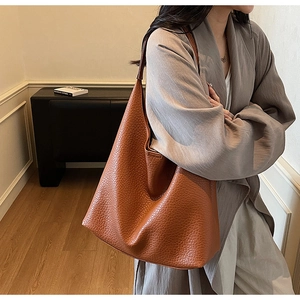 Detailed texture of caramel brown lychee leather tote bag worn by a model in interior