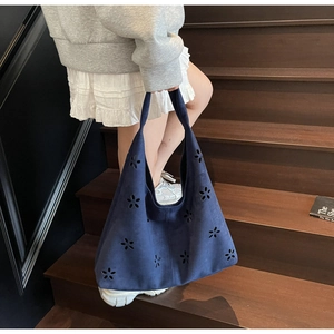 Detail of navy blue suede tote bag featuring laser-cut floral patterns and wide shoulder strap