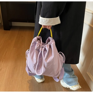 Dettaglio della borsa a secchiello in nylon viola con manico giallo e tracolla larga