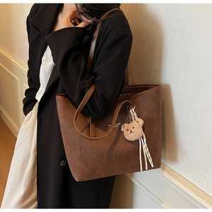 Detail of brown suede tote bag with white lettering and cute bear plush charm accessory