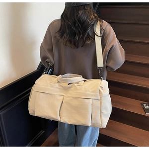 Detail of cream canvas travel bag with side pockets and adjustable shoulder strap on model