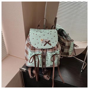 Detail view of mint green and brown plaid backpack featuring star patterns and ribbon ties