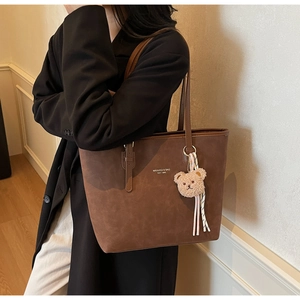 Detail of dark brown suede tote bag featuring a cute bear charm and striped ribbon accent
