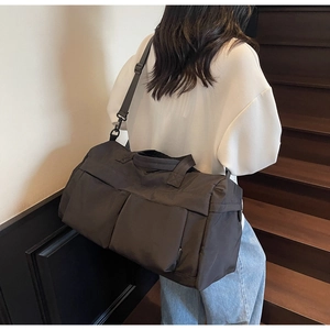 Rear view of a black nylon travel bag with dual pockets on a modern indoor staircase