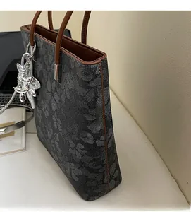Detail of dark grey tote bag with floral texture, brown leather handle and silver dog charm