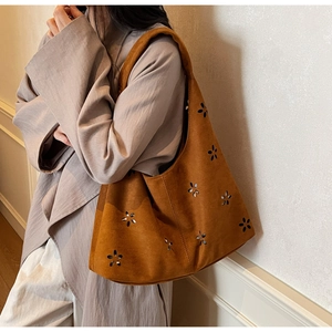 Detail of caramel brown suede shoulder bag featuring intricate laser-cut floral patterns