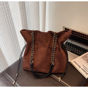 Détail du sac seau en daim marron avec anse en chaîne sur un banc en cuir