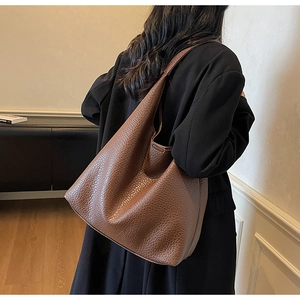 Detailed view of brown grain leather tote bag worn by a model in a modern room