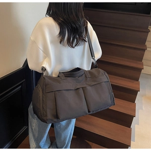Rear view of model wearing a large black nylon travel bag on modern wooden stairs