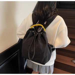 Dettaglio di uno zaino nero con coulisse e manico intrecciato giallo indossato da modella
