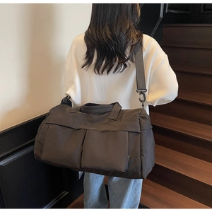 Detail showing high-capacity black travel bag with wide shoulder strap and front pockets