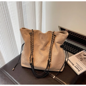 Détail du sac seau en daim beige avec chaîne dorée et logo de mode imprimé