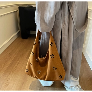 Detail of hollow floral laser-cut pattern on brown suede leather crescent shoulder bag